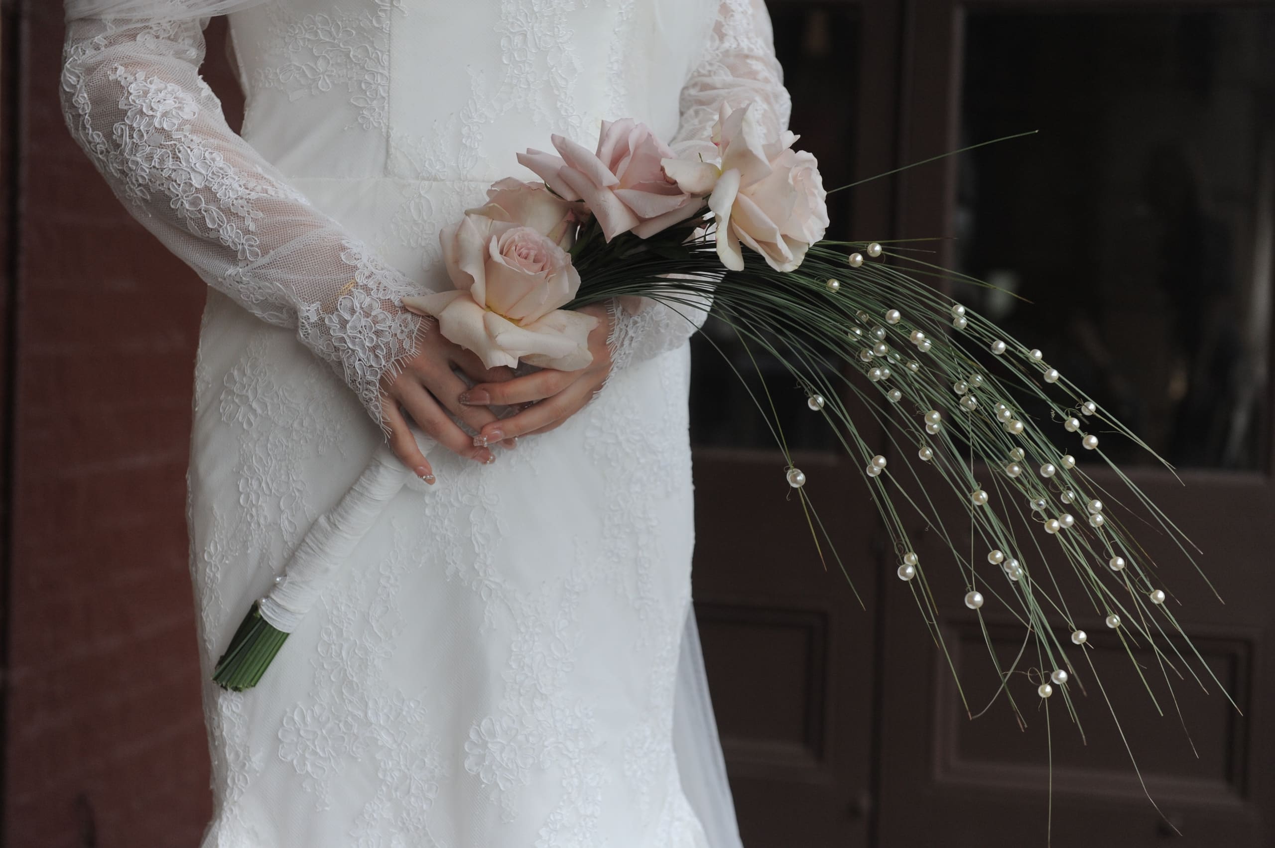 Hands holding a blush rose bouquet with pearl-tipped stems