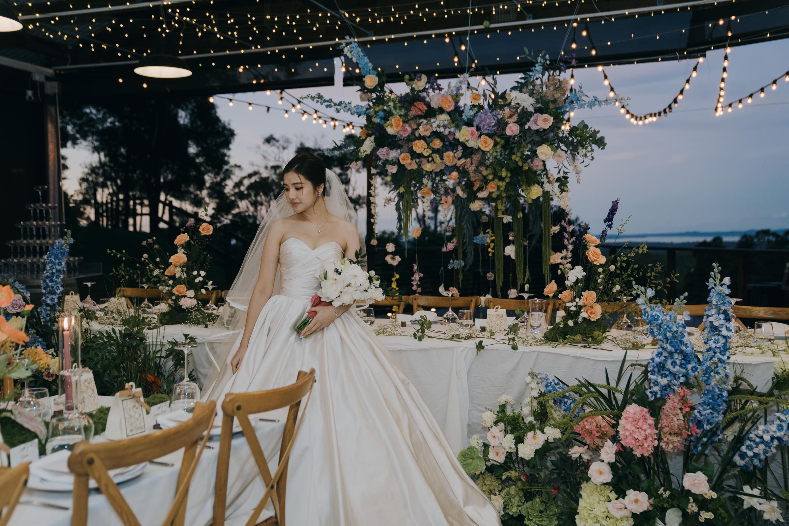 A bride among abundant pastel florals beneath a floral arch at dusk