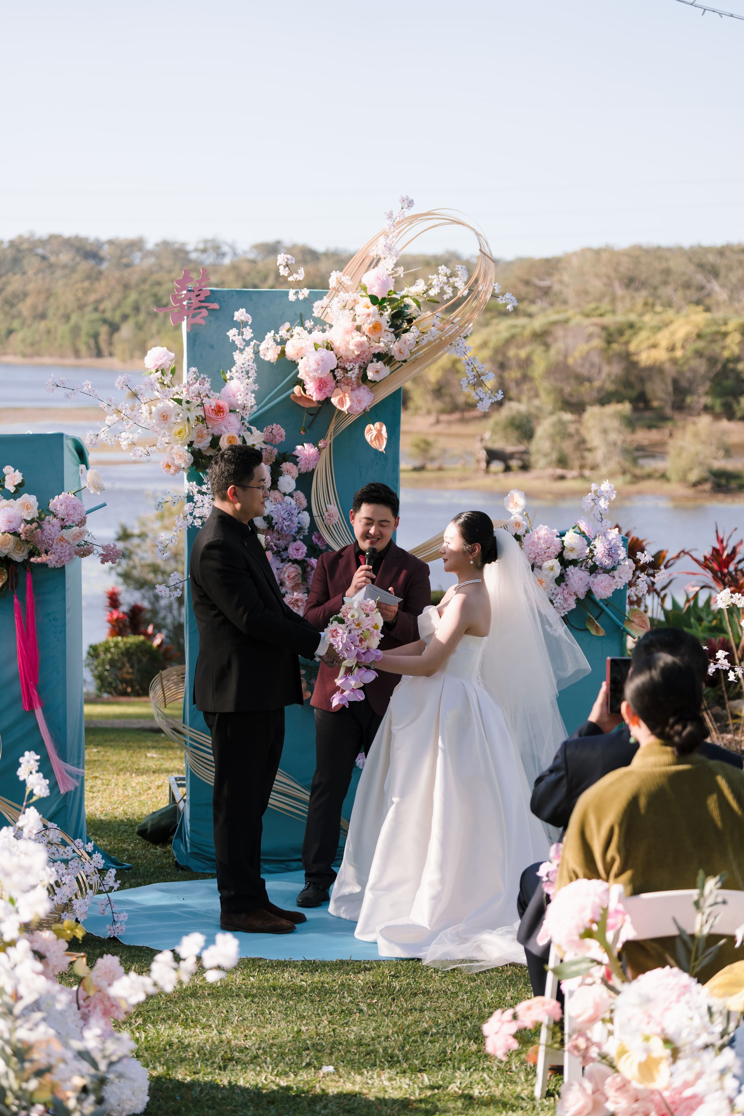 The couple at the lakeside ceremony beneath pink and white florals